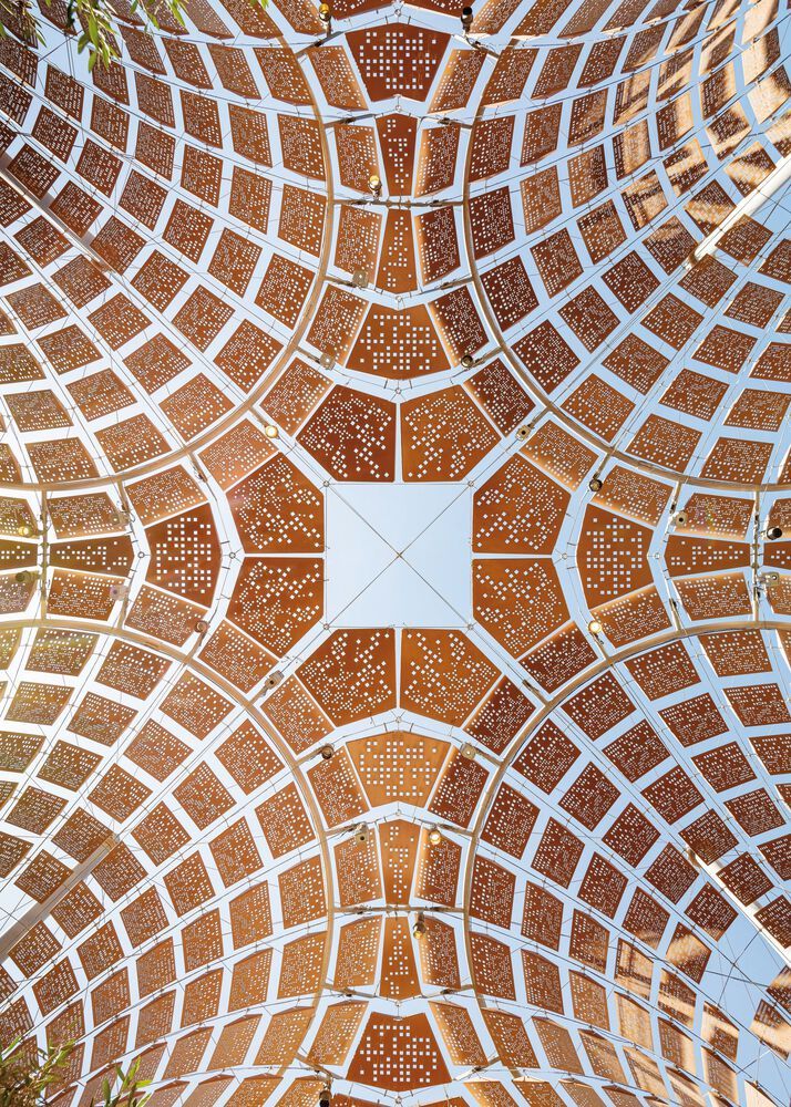 A perforated copper-toned dome seen from below, open to the sky at its centre